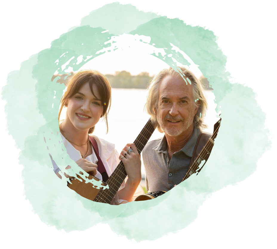 John and Cass holding guitars in front of a lake